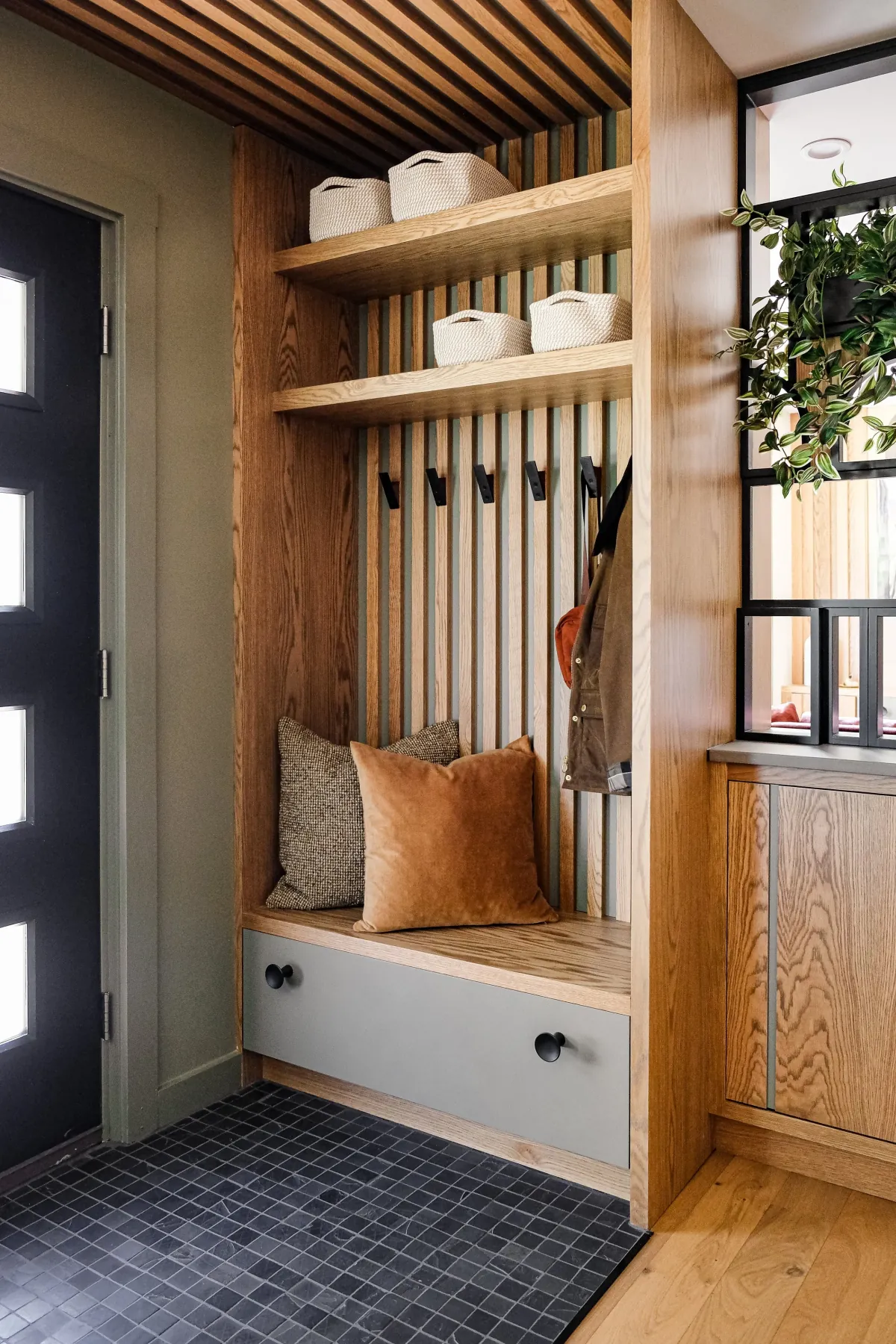 Built-in white-oak entry bench with slat wall, coat hooks, cubbies and slatted soffit