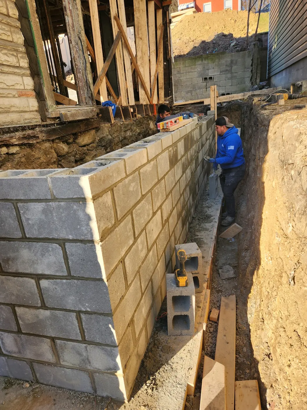 Mason laying a CMU block foundation wall in a Pittsburgh excavation
